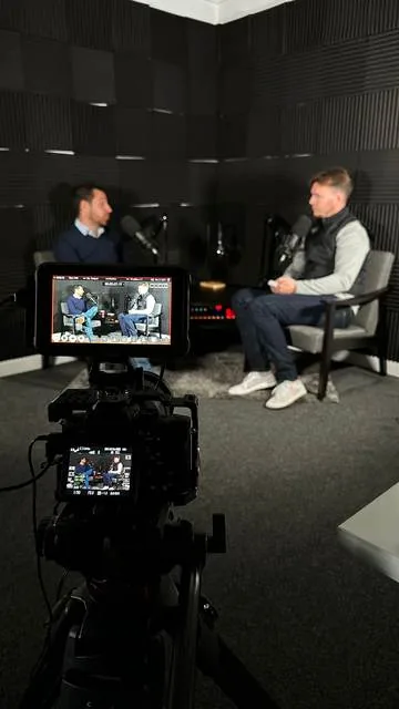 A podcast episode being recorded: two people talking in a sound-treated studio, seen past the camera